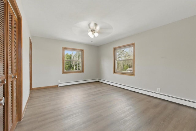 unfurnished bedroom featuring a closet, baseboards, a baseboard heating unit, and wood finished floors