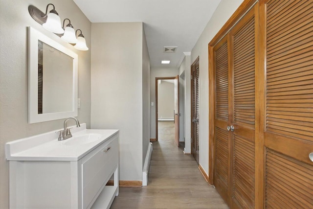 interior space with visible vents, light wood-type flooring, a sink, baseboards, and a baseboard radiator