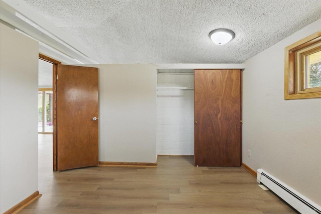 unfurnished bedroom featuring baseboards, baseboard heating, a textured ceiling, and wood finished floors