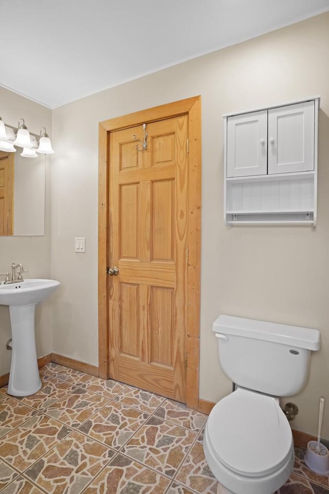 bathroom with a sink, baseboards, toilet, and stone finish flooring