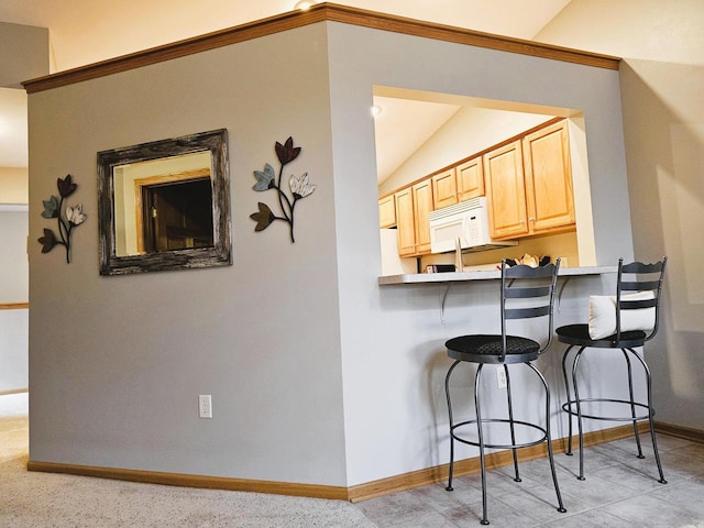 850 Evergreen Dr Unit 8, Hartford, WI 53027 - kitchen with light brown cabinetry, white microwave, baseboards, lofted ceiling, and a kitchen bar