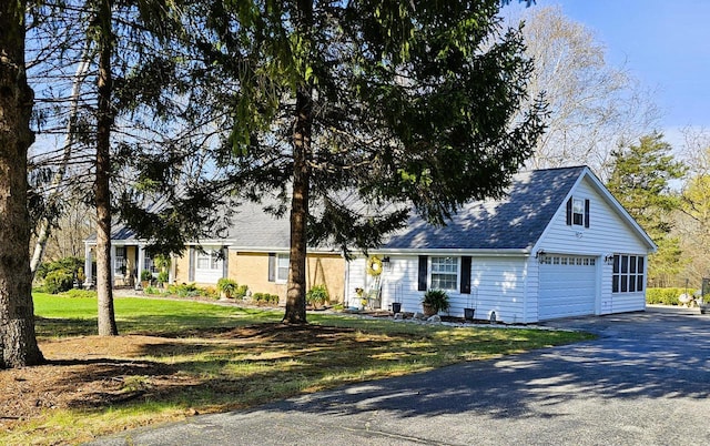 view of front of property featuring aphalt driveway, roof with shingles, and a front yard