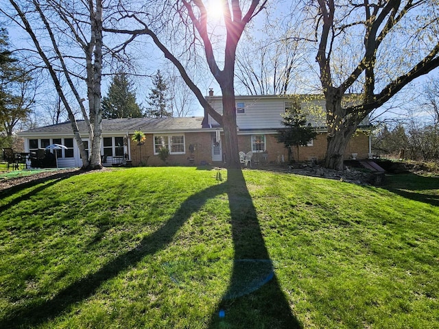 rear view of property with a chimney, a yard, and brick siding