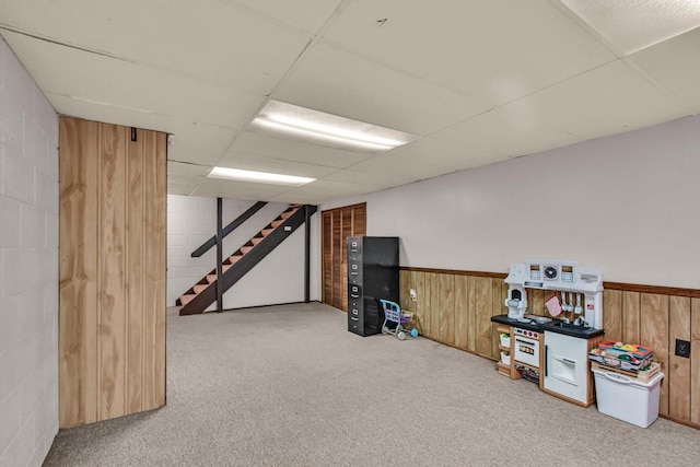 game room with carpet flooring, wood walls, a drop ceiling, and a wainscoted wall