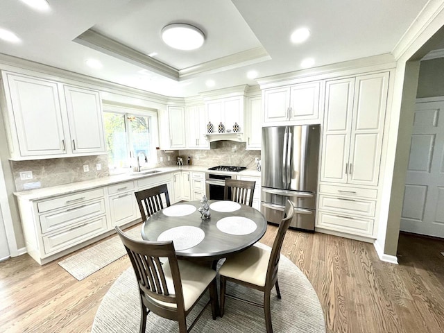 kitchen featuring a tray ceiling, crown molding, a sink, light countertops, and stainless steel appliances