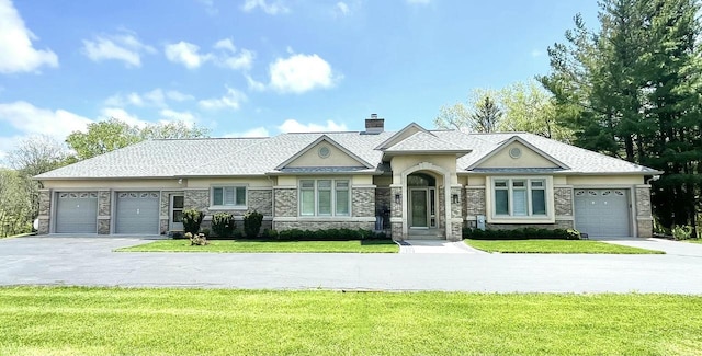 view of front of property with an attached garage, a chimney, a front yard, and aphalt driveway