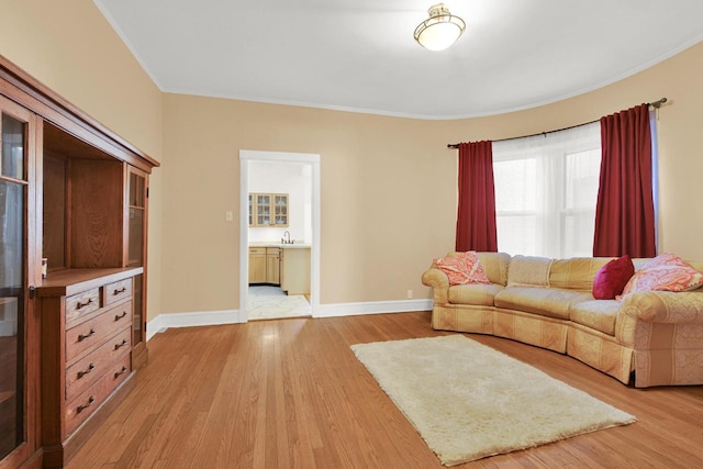 living area with crown molding, baseboards, and light wood finished floors