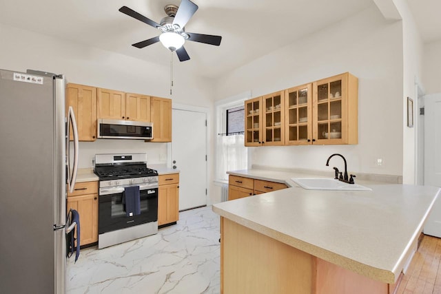 kitchen featuring a sink, a peninsula, light brown cabinetry, a ceiling fan, and stainless steel appliances