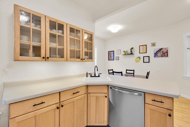kitchen featuring a peninsula, light brown cabinetry, glass insert cabinets, a sink, and dishwasher