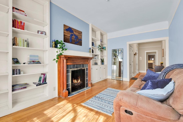 living area featuring a fireplace with flush hearth, built in features, and wood finished floors