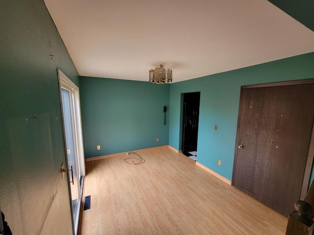 unfurnished bedroom featuring baseboards, a chandelier, light wood-style flooring, and visible vents