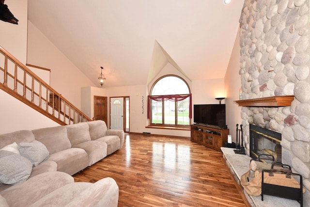 living room with a stone fireplace, stairs, high vaulted ceiling, and hardwood / wood-style flooring