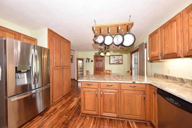 kitchen with a peninsula, light stone countertops, dark wood-style floors, brown cabinets, and appliances with stainless steel finishes