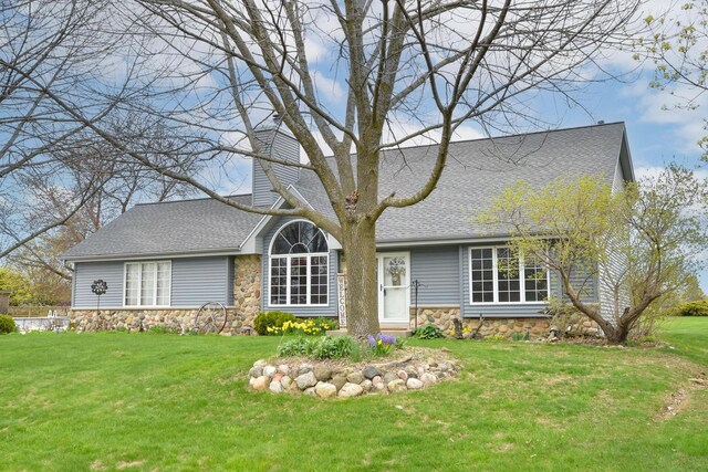 view of front of home featuring a shingled roof, a front yard, and stone siding
