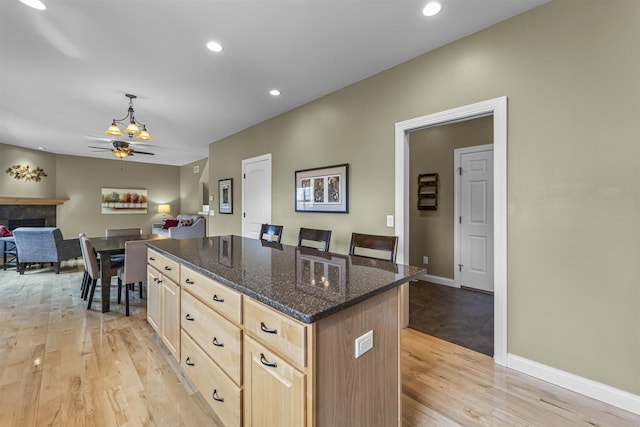 kitchen featuring light brown cabinetry, a fireplace, a center island, a ceiling fan, and light wood-style flooring
