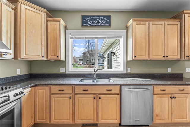 kitchen with a sink, appliances with stainless steel finishes, light brown cabinets, and dark stone countertops