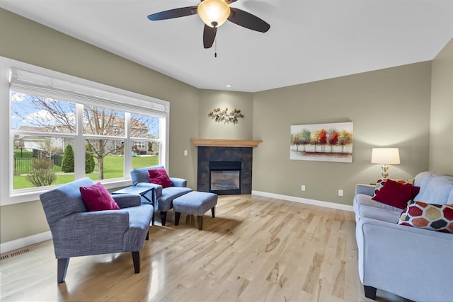 living area with visible vents, a fireplace, light wood-style floors, baseboards, and a ceiling fan