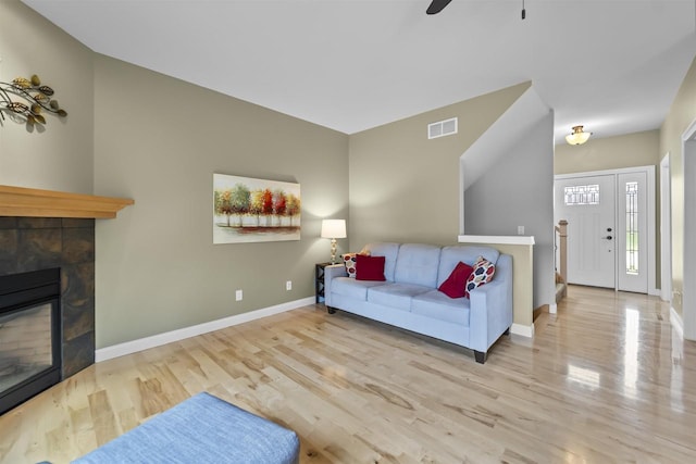 living area featuring visible vents, a glass covered fireplace, wood finished floors, baseboards, and ceiling fan