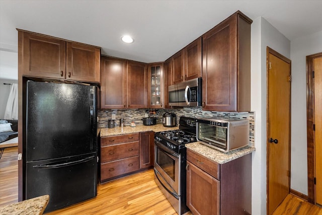 kitchen featuring appliances with stainless steel finishes, light stone counters, light wood-style floors, a toaster, and backsplash