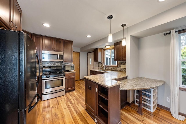 kitchen with light wood-style floors, a sink, appliances with stainless steel finishes, and a peninsula