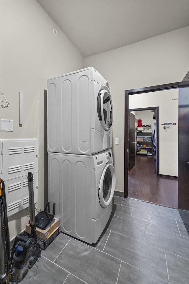 laundry room featuring baseboards, laundry area, stacked washing maching and dryer, and tile patterned floors