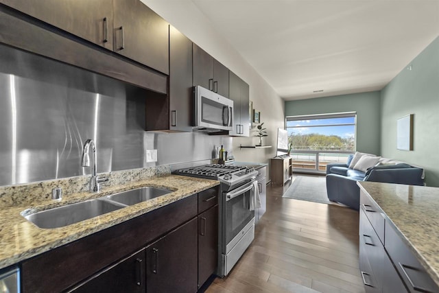 kitchen featuring appliances with stainless steel finishes, a sink, light stone counters, open floor plan, and dark wood-type flooring