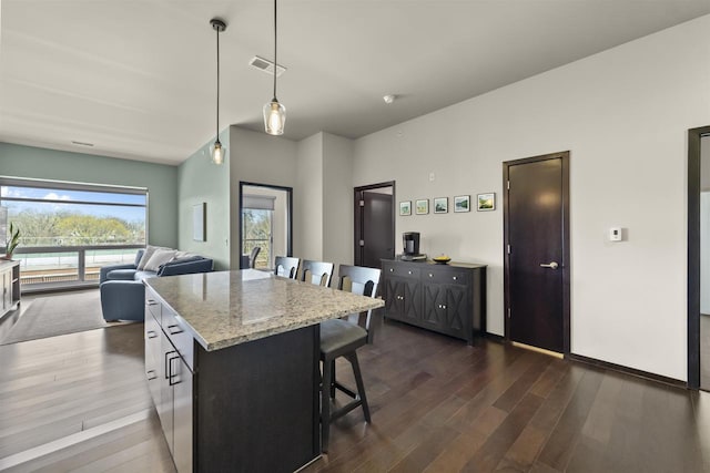 kitchen with light stone countertops, dark wood finished floors, a center island, a kitchen bar, and visible vents