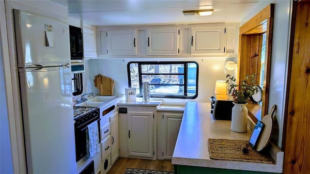 kitchen featuring black microwave, light countertops, freestanding refrigerator, white cabinetry, and range with gas cooktop