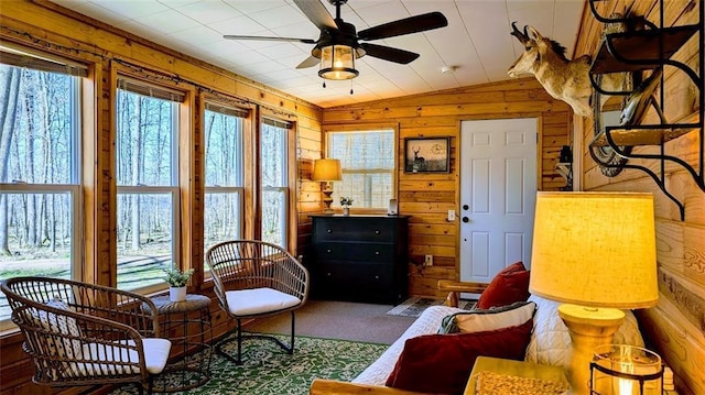 living area featuring carpet floors, a ceiling fan, wooden walls, and a healthy amount of sunlight