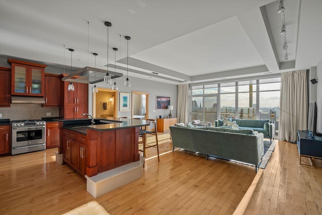 kitchen featuring dark countertops, gas stove, light wood finished floors, open floor plan, and under cabinet range hood