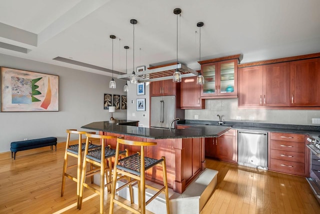kitchen with a breakfast bar, glass insert cabinets, tasteful backsplash, light wood finished floors, and appliances with stainless steel finishes