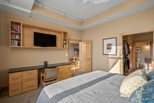 bedroom featuring rail lighting, built in desk, and dark colored carpet