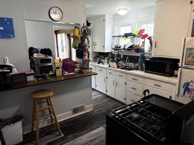 kitchen featuring black microwave, white cabinets, dark wood-style flooring, and visible vents