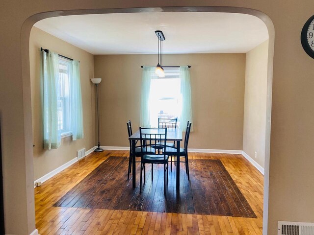 dining area featuring arched walkways, baseboards, visible vents, and hardwood / wood-style flooring