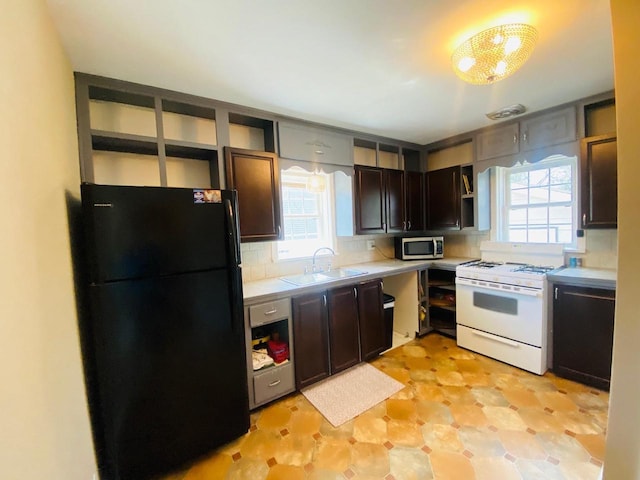 kitchen featuring freestanding refrigerator, white range with gas cooktop, stainless steel microwave, a sink, and a wealth of natural light