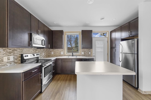 kitchen with stainless steel appliances, dark brown cabinetry, a sink, and light wood-style flooring