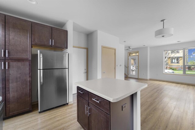 kitchen with freestanding refrigerator, dark brown cabinetry, open floor plan, light wood-type flooring, and light countertops