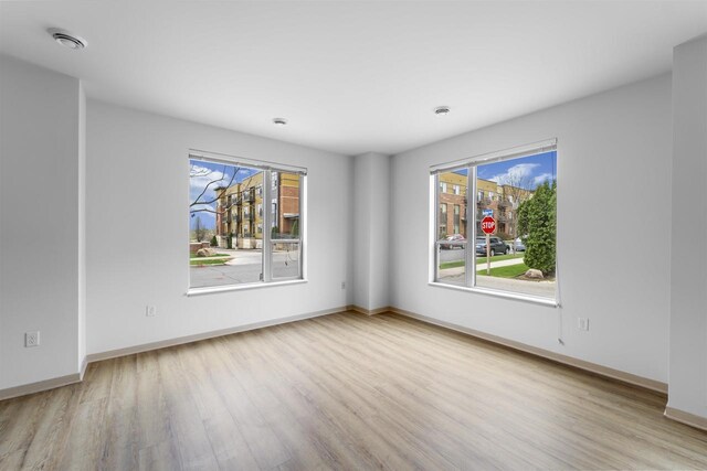 empty room with a healthy amount of sunlight, baseboards, wood finished floors, and visible vents