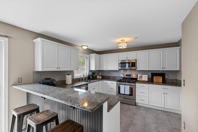 kitchen with white cabinets, appliances with stainless steel finishes, a sink, a peninsula, and tasteful backsplash