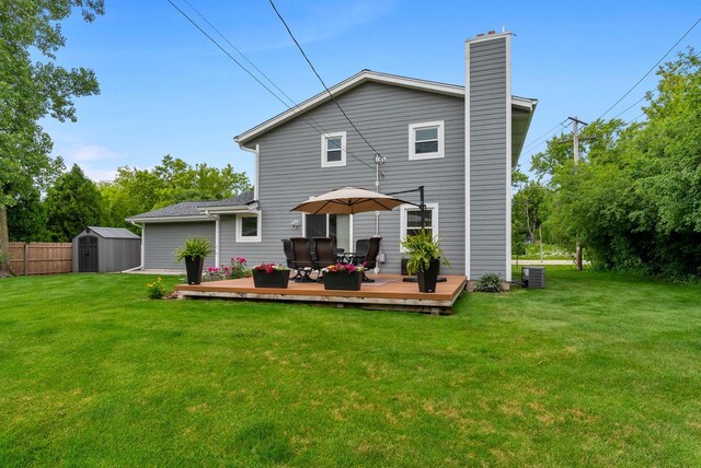 rear view of property with a chimney, a storage shed, a wooden deck, an outdoor structure, and a yard