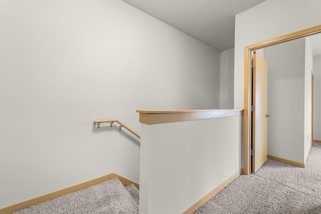 hall featuring carpet flooring, baseboards, and an upstairs landing
