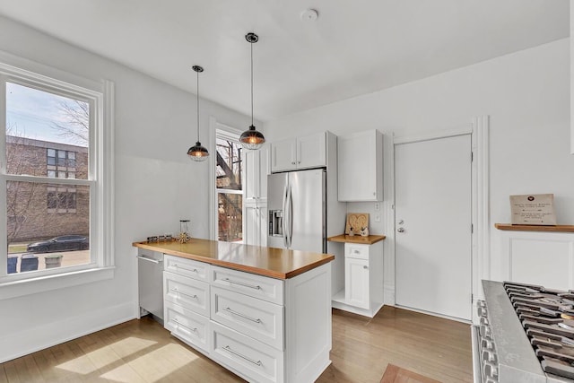 kitchen with a peninsula, white cabinetry, light wood finished floors, hanging light fixtures, and stainless steel appliances