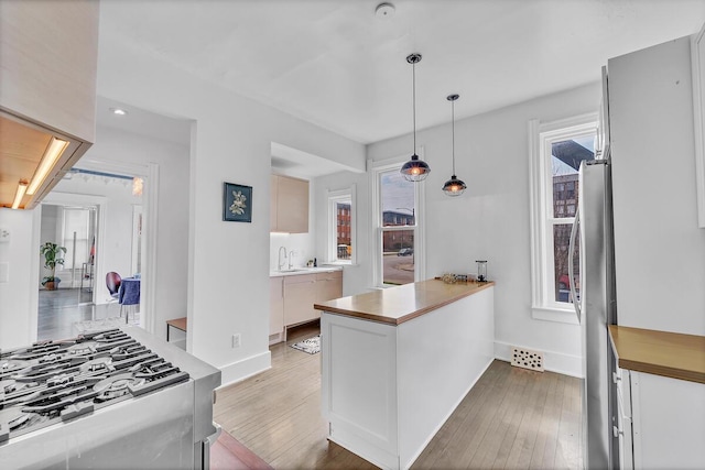 kitchen with a peninsula, hardwood / wood-style floors, baseboards, appliances with stainless steel finishes, and decorative light fixtures