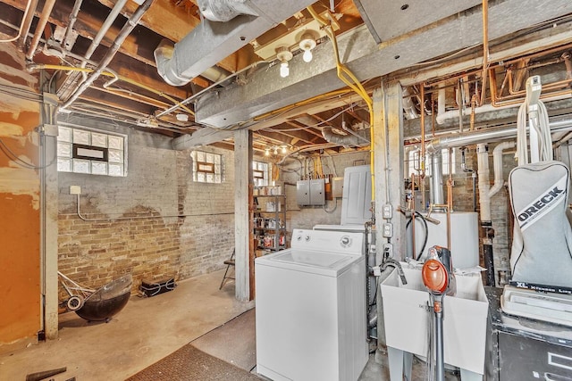 below grade area featuring a sink, electric panel, washer / clothes dryer, and brick wall