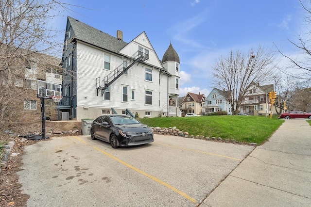 exterior space featuring a chimney, roof with shingles, a residential view, uncovered parking, and a yard