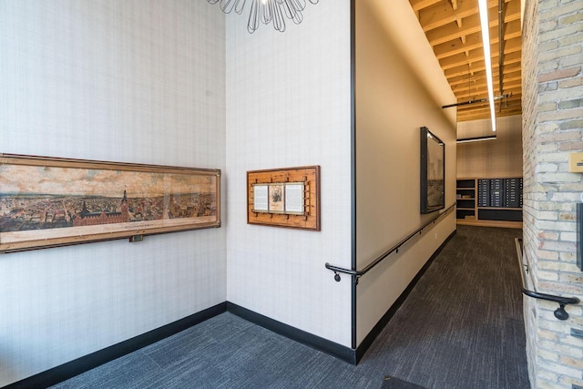 hallway with wallpapered walls, dark colored carpet, baseboards, and a notable chandelier
