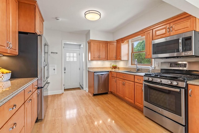 kitchen featuring light stone countertops, baseboards, a sink, light wood finished floors, and stainless steel appliances
