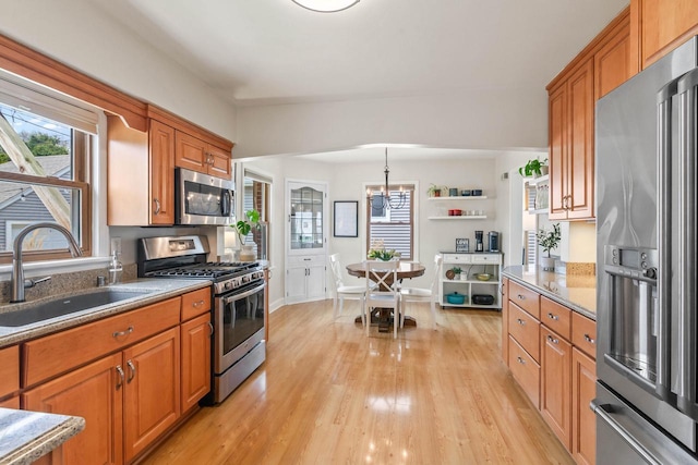 kitchen featuring plenty of natural light, brown cabinets, a sink, stainless steel appliances, and light wood-style flooring