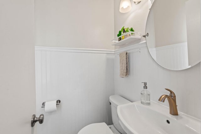 bathroom with a sink, a wainscoted wall, a decorative wall, and toilet