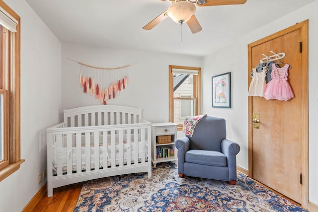 bedroom with baseboards, ceiling fan, a crib, and wood finished floors